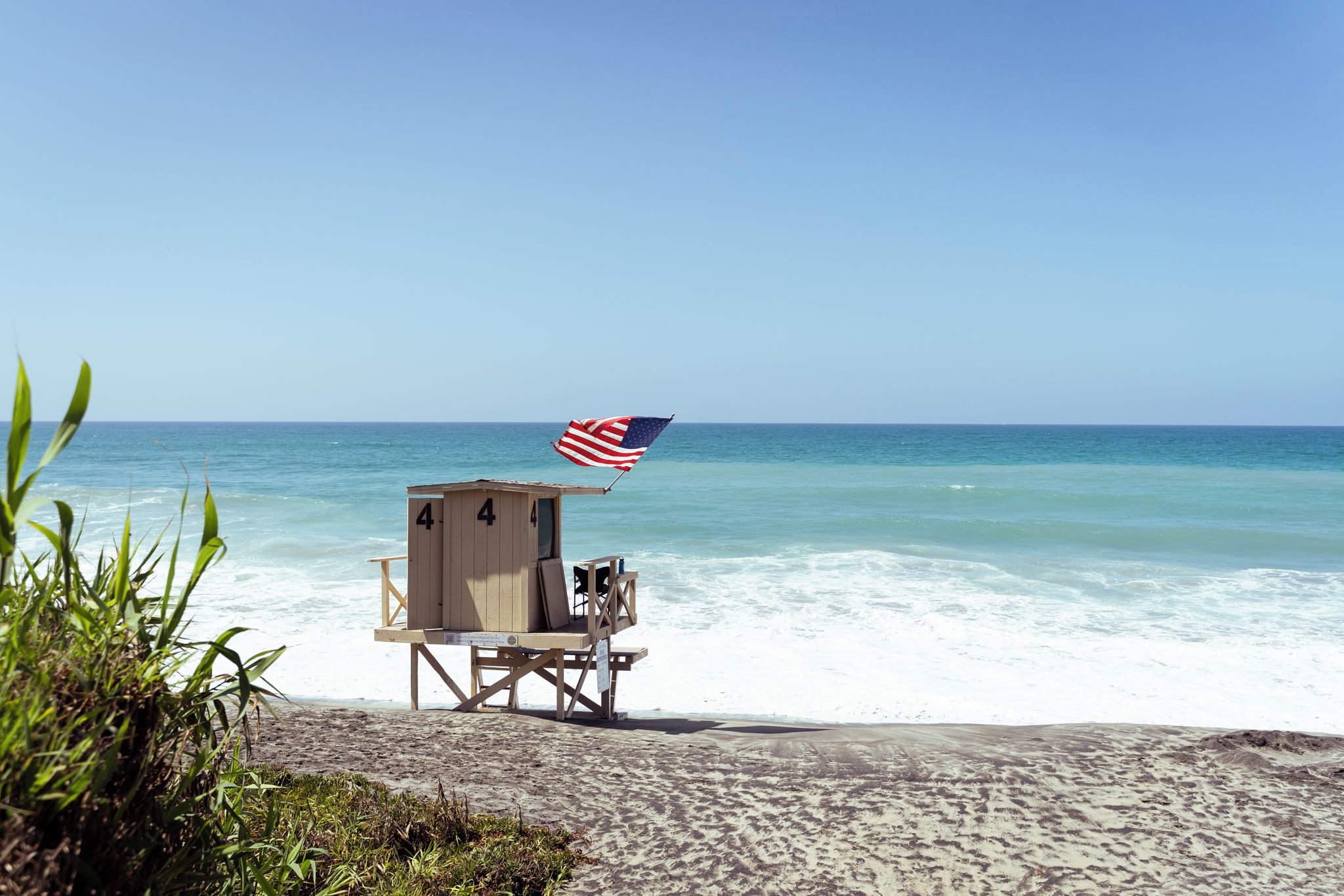 A beach lifeguard tower with an American flag, situated on a sandy beach with ocean waves in the background.