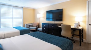 A hotel room with two beds, a desk, a chair, a television, and a lamp.