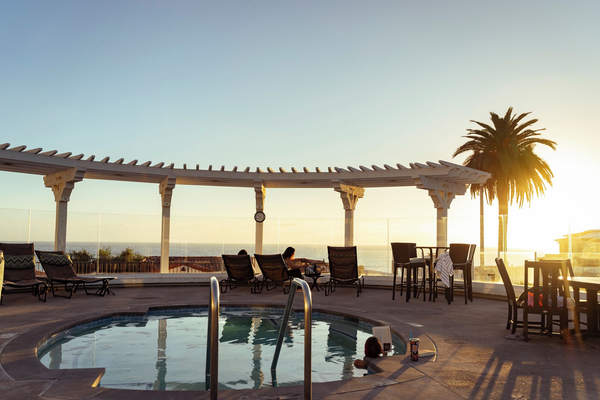 A poolside area with lounge chairs, a pool, and a view of the ocean.