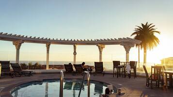 A poolside area with lounge chairs, a pool, and a view of the ocean.