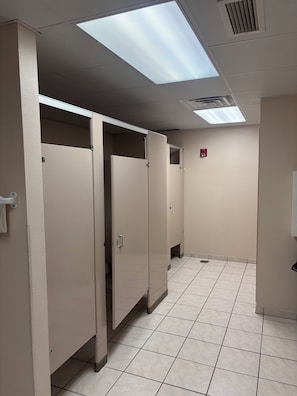Un couloir avec des toilettes, un détecteur d’incendie et un sol carrelé.