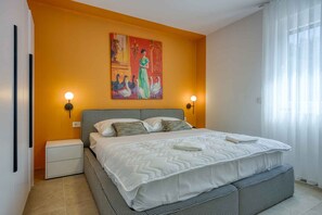 Ein Schlafzimmer mit einem großen Bett, zwei Nachttischen, einem Bild an der Wand und einem Fenster mit Vorhängen.