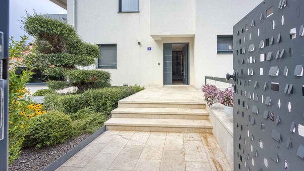 A modern building with a flat facade, a set of steps leading to a door, and a metal gate with cut-out panels. - Holiday property in typical regional style (Poreč)