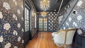 Un pasillo con papel tapiz floral, una araña, una escalera y una silla antigua.