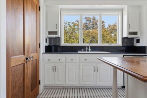 A kitchen with white cabinets, a black countertop, a window with a view of trees, and a wooden door.
