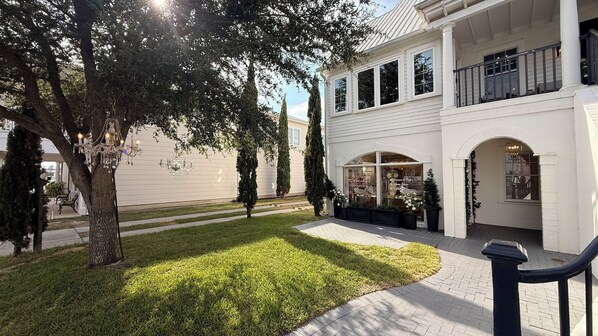 A white building with a storefront, a paved walkway, and a well-maintained lawn.