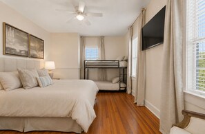 A bedroom with a bed, a bunk bed, a ceiling fan, a TV, and a window with curtains.