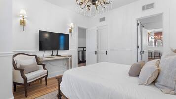 Ein Schlafzimmer mit einem großen Bett, einem Schreibtisch, einem Sessel, einem Fernseher und einer Kandelaber.