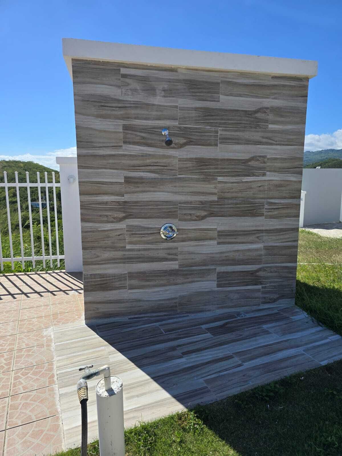 Ducha exterior moderna con pared de textura de piedra, grifo de metal y manija de metal.