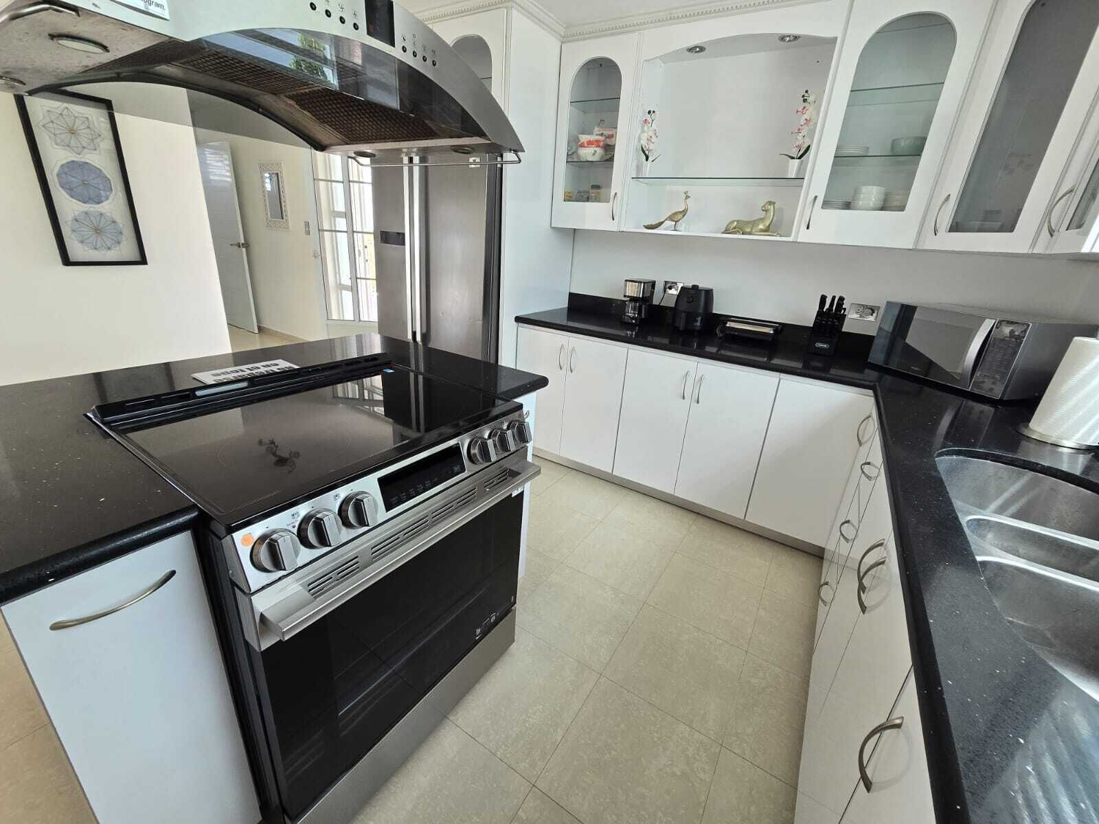 Una cocina con tope negro, armarios blancos y una campana extractora de acero inoxidable.