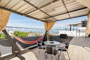 Ein überdachter Außenbereich mit Tisch und Stühlen, einer Hängematte und Blick auf die Stadt.