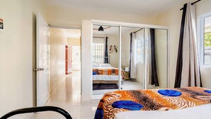 Quarto de hotel com cama, uma cadeira, um guarda-roupa e um banheiro visível por uma porta aberta.