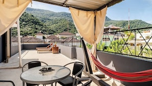 Um terraço com mesa e cadeiras, uma rede e vista para uma paisagem montanhosa.