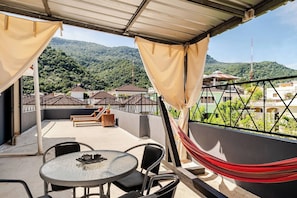 Eine Terrasse mit Tisch, Stühlen und einer Hängematte, mit Blick auf eine gebirgige Landschaft.