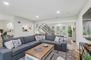 Ein modernes Wohnzimmer mit einem grauen Ecksofa, einem Holztisch und einer Treppe, die in eine obere Ebene führt.