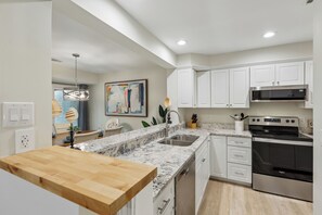 Eine moderne Küche mit weißen Schränken, einer Granitarbeitsplatte, Edelstahlgeräten und einem Essbereich mit einem Holztisch und Stühlen.