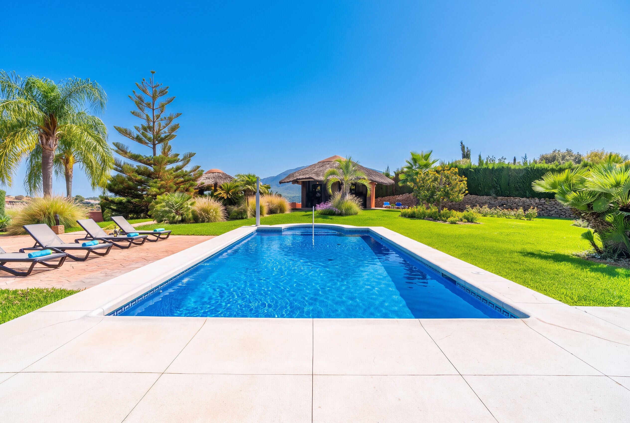 Ein Swimmingpool mit Liegestühlen und einer Struktur mit Reetdach.