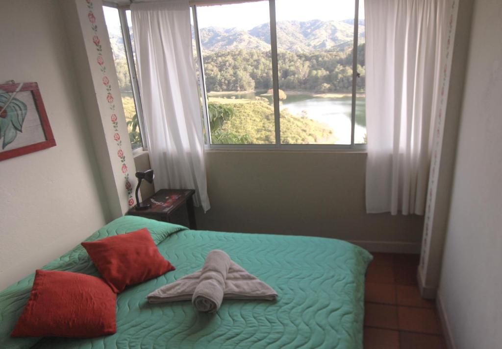 Une chambre avec un lit, une fenêtre avec des rideaux, un tableau encadré au mur et une vue sur un lac et des montagnes.