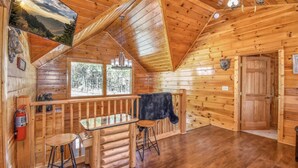 Ein Holzblockhaus-Interieur mit Holzbalkendecke, einem Essbereich mit Hocker, einer schwarzen Kuh an der Wand und einem Feuerlöscher.