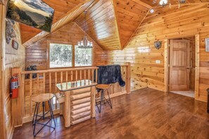 Ein Holzblockhaus-Interieur mit Holzbalkendecke, einem Essbereich mit Hocker, einer schwarzen Kuh an der Wand und einem Feuerlöscher.