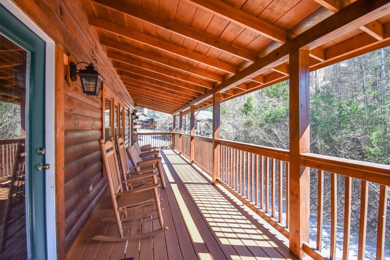 Una terraza de madera con barandilla, una puerta y vistas a árboles.