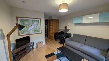 Un salon moderne avec un téléviseur à écran plat, un canapé gris, une table basse, un plancher en bois et une carte accrochée au mur.