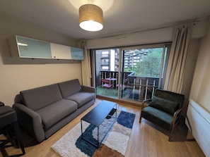 Un salon moderne avec un canapé, un fauteuil et une table basse. Une porte-fenêtre coulissante donne accès à un balcon extérieur équipé d’un ensemble de mobilier de jardin.