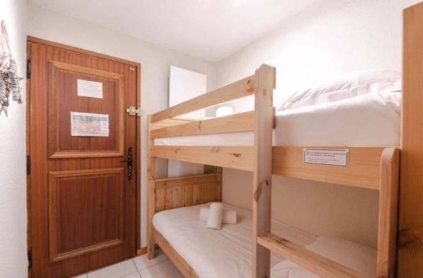 Une chambre avec un lit superposé, une porte en bois et une petite affiche accrochée à la porte.
