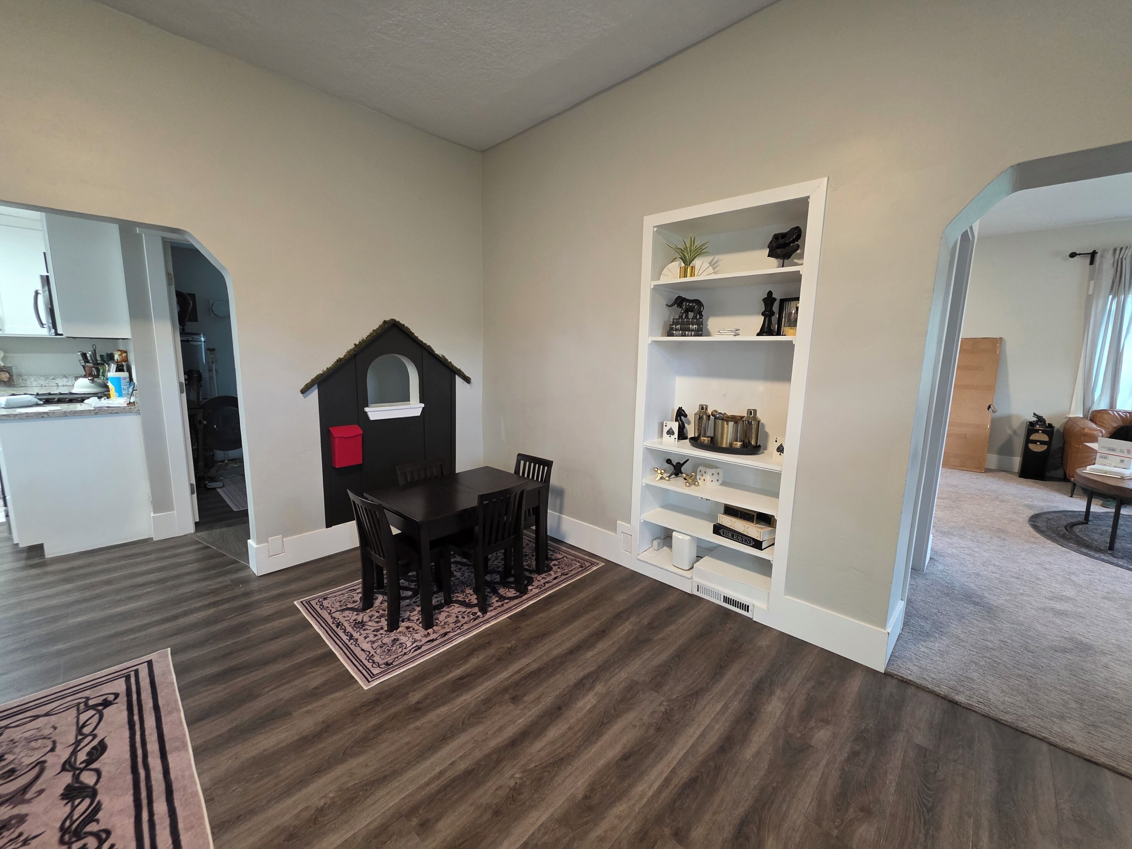 Ein Zimmer mit Esstisch, Stühlen, einem Bücherregal und einem kleinen Spielhäuschen.