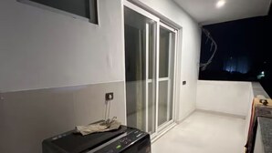 Una habitación con puerta corrediza de vidrio que da a un balcón, un electrodoméstico negro en el suelo y un ventanal con vista al cielo nocturno.
