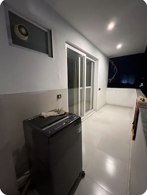 A room with a sliding glass door leading to a balcony, a black appliance on the floor, and a small window with a view of the night sky.