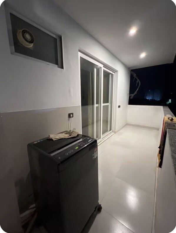 Une pièce dotée d’une porte-fenêtre coulissante donnant sur un balcon, d’un appareil noir posé sur le sol et d’une petite fenêtre offrant une vue sur le ciel nocturne.