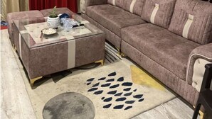Una sala de estar con un sofá modular, una mesa de centro de vidrio, una planta en maceta y un adorno de pared.