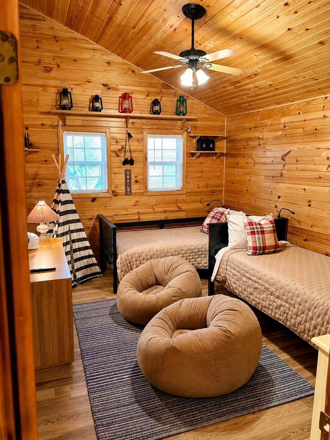 A cozy cabin-style room with two beds, a ceiling fan, and a window with blinds.