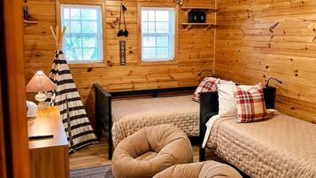 A cozy cabin-style room with two beds, a ceiling fan, and a window with blinds.