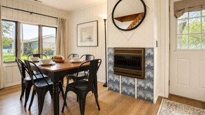 Uma área de refeições com uma mesa de madeira e cadeiras pretas, uma lareira com detalhes em azulejos decorativos e um espelho grande na parede.