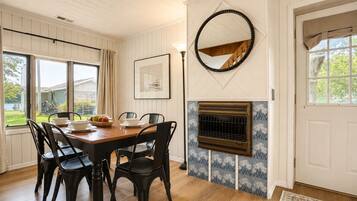 A dining area with a wooden table and black chairs, a fireplace with a decorative tile surround, and a large mirror on the wall.