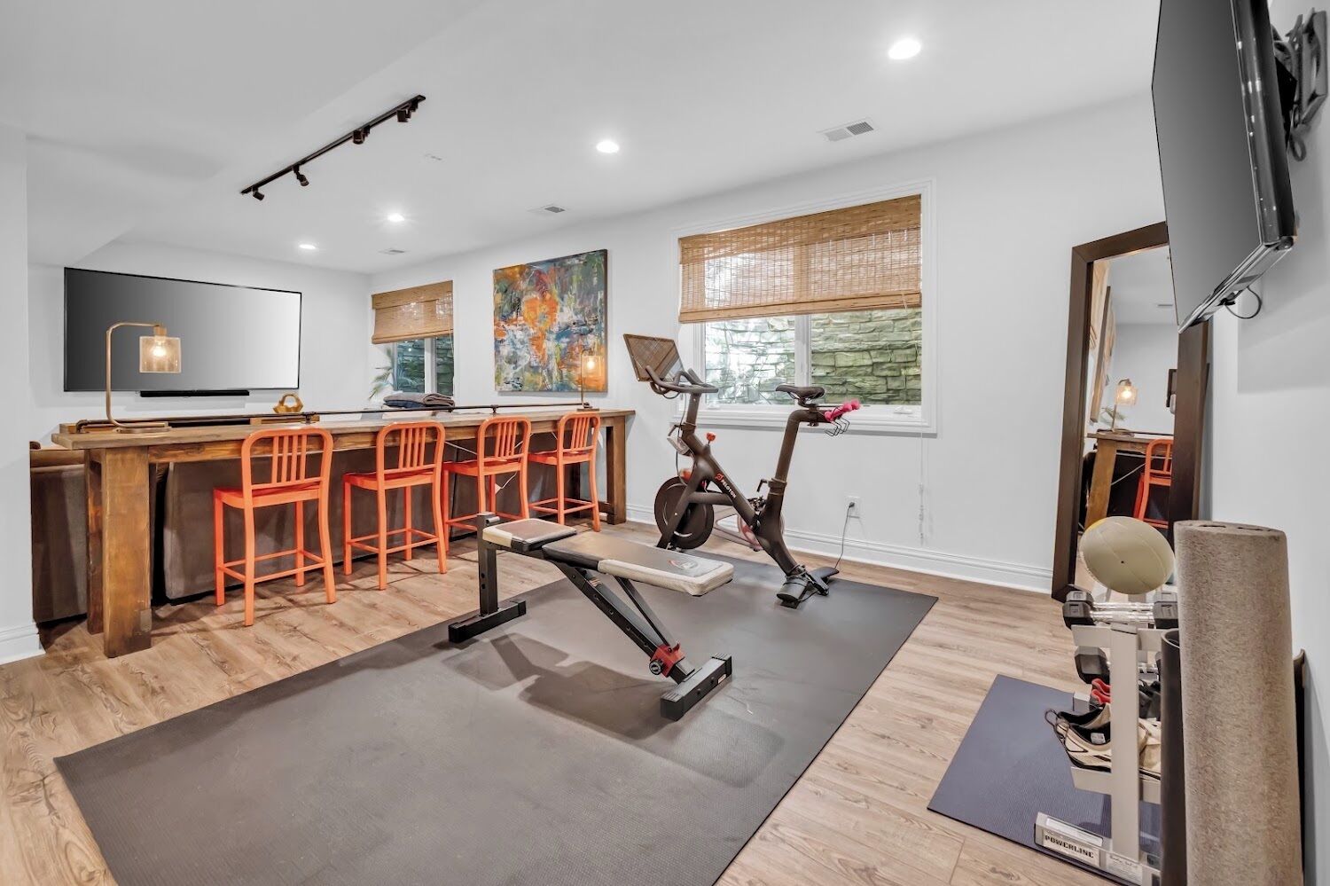 A modern home gym with exercise equipment, a dining area with a bar, and artwork on the walls.