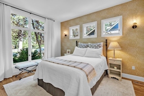 Une chambre à coucher avec un lit, des tables de chevet, une fenêtre avec des rideaux et une vue sur la verdure à l’extérieur.