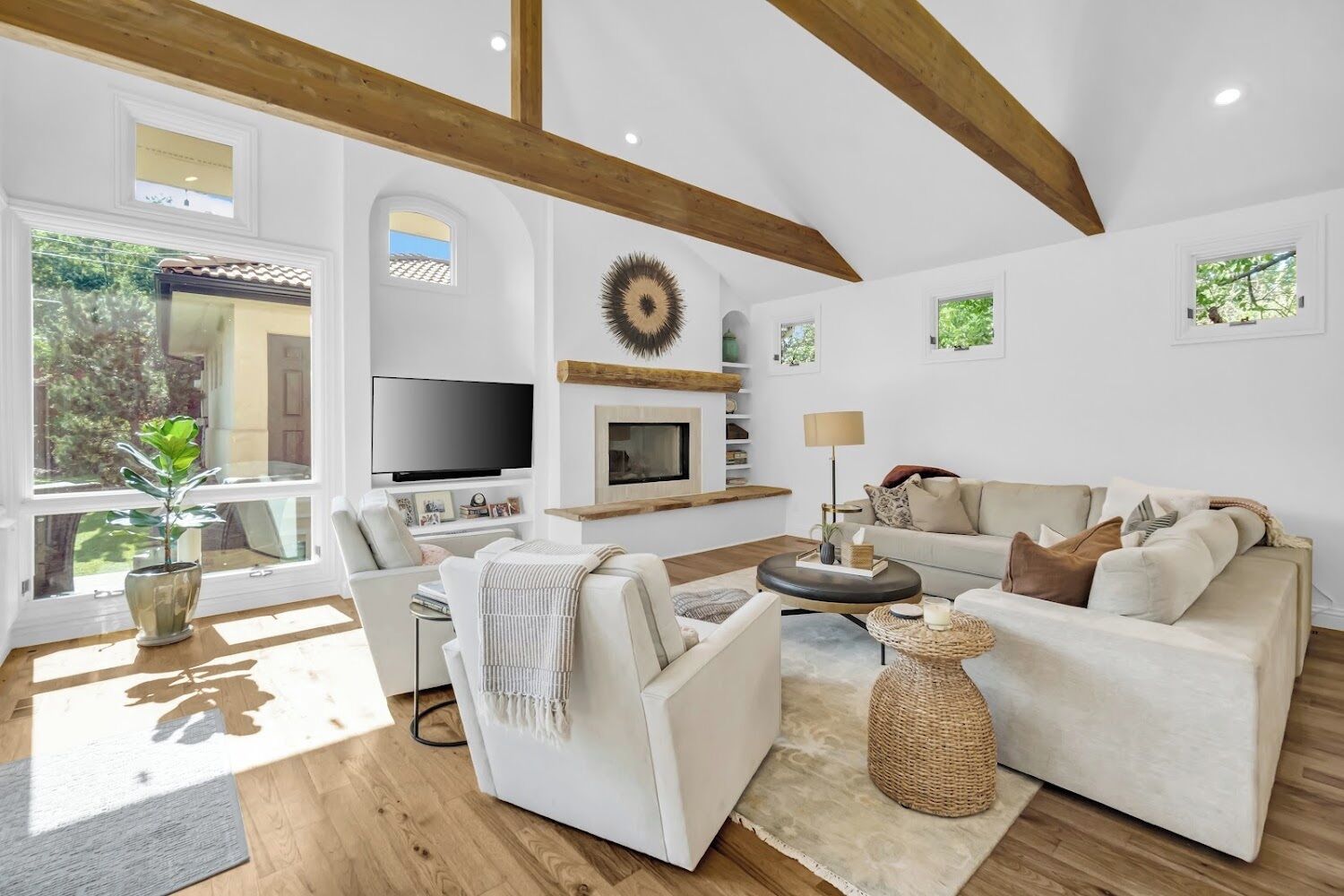Een ruime woonkamer met een open haard, een televisie en een groot raam met uitzicht op groen.