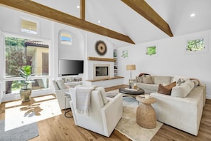 A spacious living room with a fireplace, a television, and a large window overlooking greenery. - North Boulder Elegance - Newlands Neighborhood (Boulder)