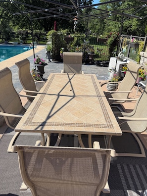 Een terras met een tafel, stoelen, een zwembad en potplanten.