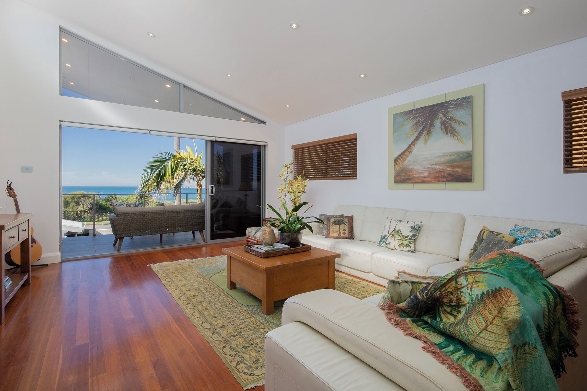 A spacious living room with a large sliding glass door leading to a balcony with a view of the ocean.