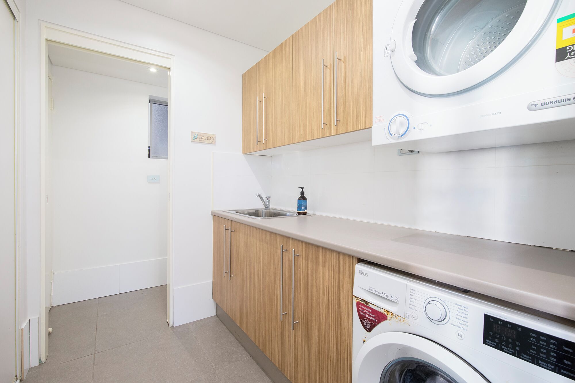 A compact laundry room with a washing machine, a sink, and wooden cabinets.