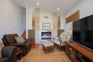 A living room with a fireplace, leather sofas, a TV, and a wooden cabinet. - Azure Horizon Beachfront Haven and Resort Style Pool (Stockton)