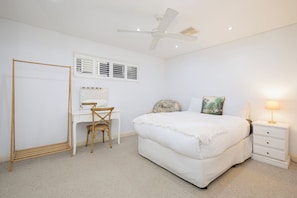 A bedroom with a bed, a desk with a chair, a vanity with a mirror, a ceiling fan, and a bedside table with a lamp. - Azure Horizon Beachfront Haven and Resort Style Pool (Stockton)