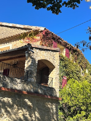 Ein Gebäude aus Stein mit einem Balkon, einer roten Tür und einem strahlend blauen Himmel.
