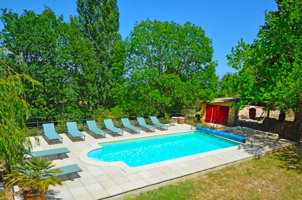 A swimming pool with lounge chairs and a small building with red shutters.