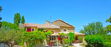 A two-story stone house with a tiled roof, a covered outdoor seating area, and a well-maintained garden.