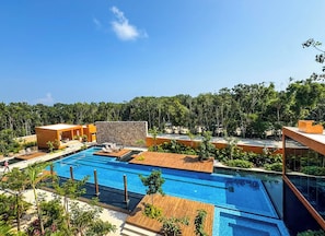 A modern resort with a large swimming pool, outdoor seating, and lush greenery. - 3BR Tulum Condo with Garden Views (Tulum)